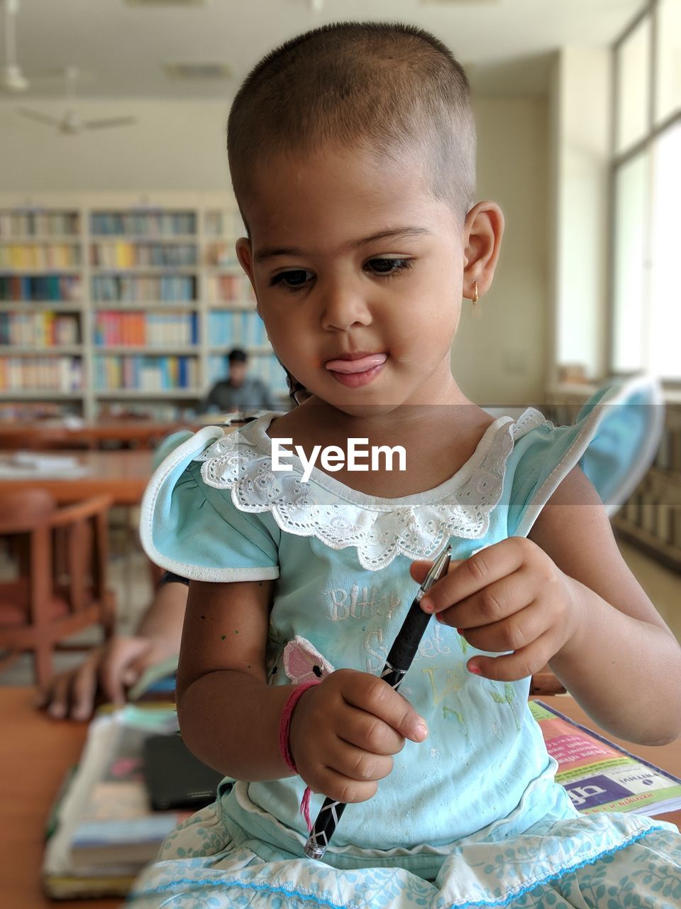 Close-up of cute girl holding pen while sitting in library