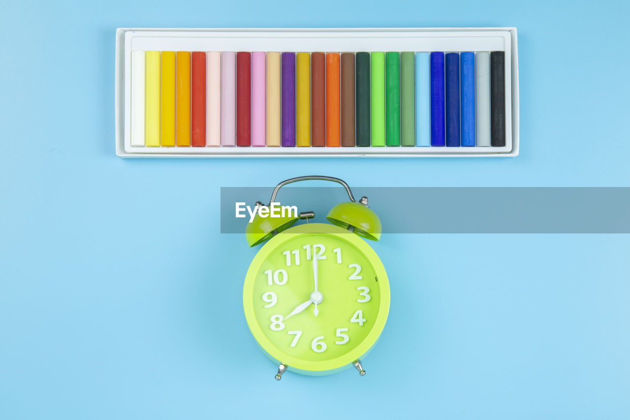 Multi colored art and craft equipment with alarm clock over blue background