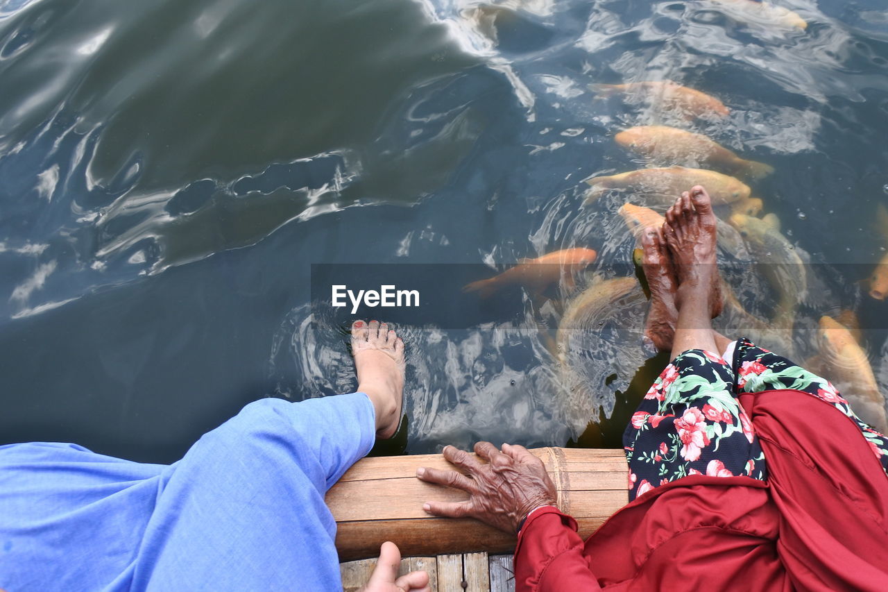 Low section of women sitting on pier over lake