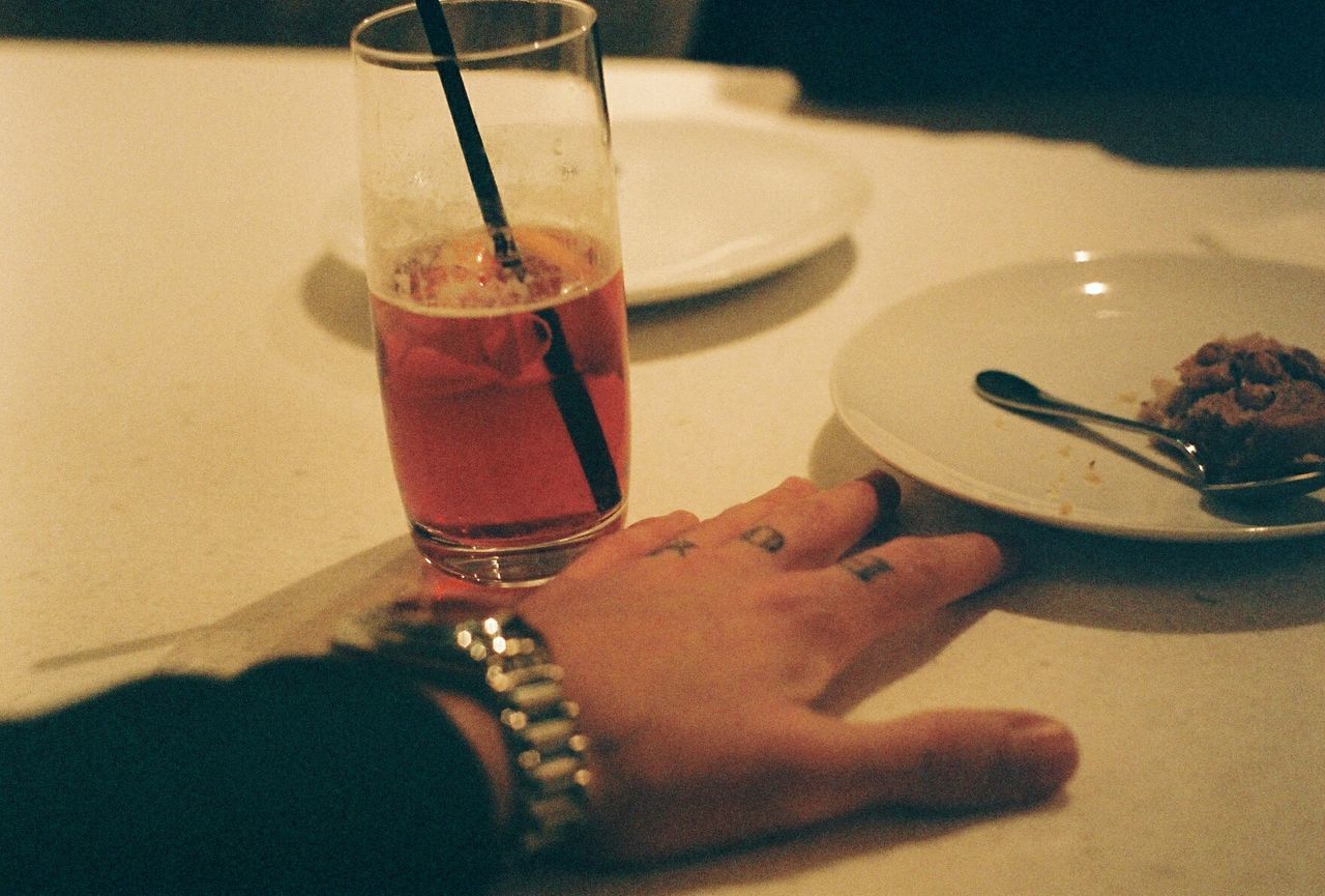 Cropped hand by drinking glass on table