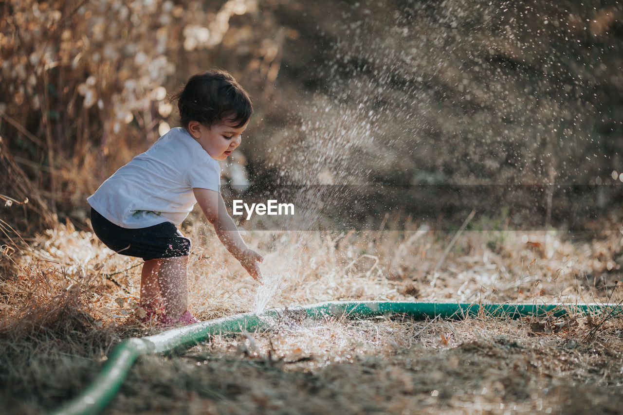 Baby girl standing by water spraying from hose on land