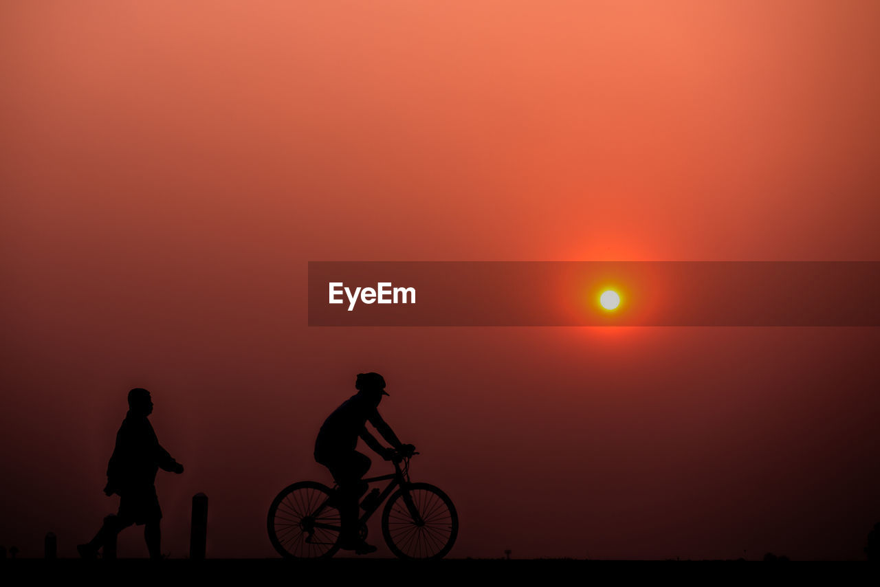 SILHOUETTE PEOPLE RIDING BICYCLES AGAINST SKY DURING SUNSET