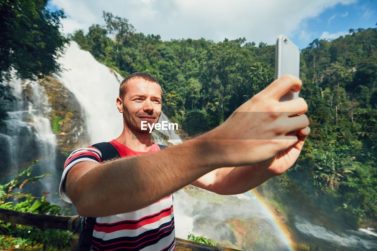 Man taking selfie while standing against waterfall