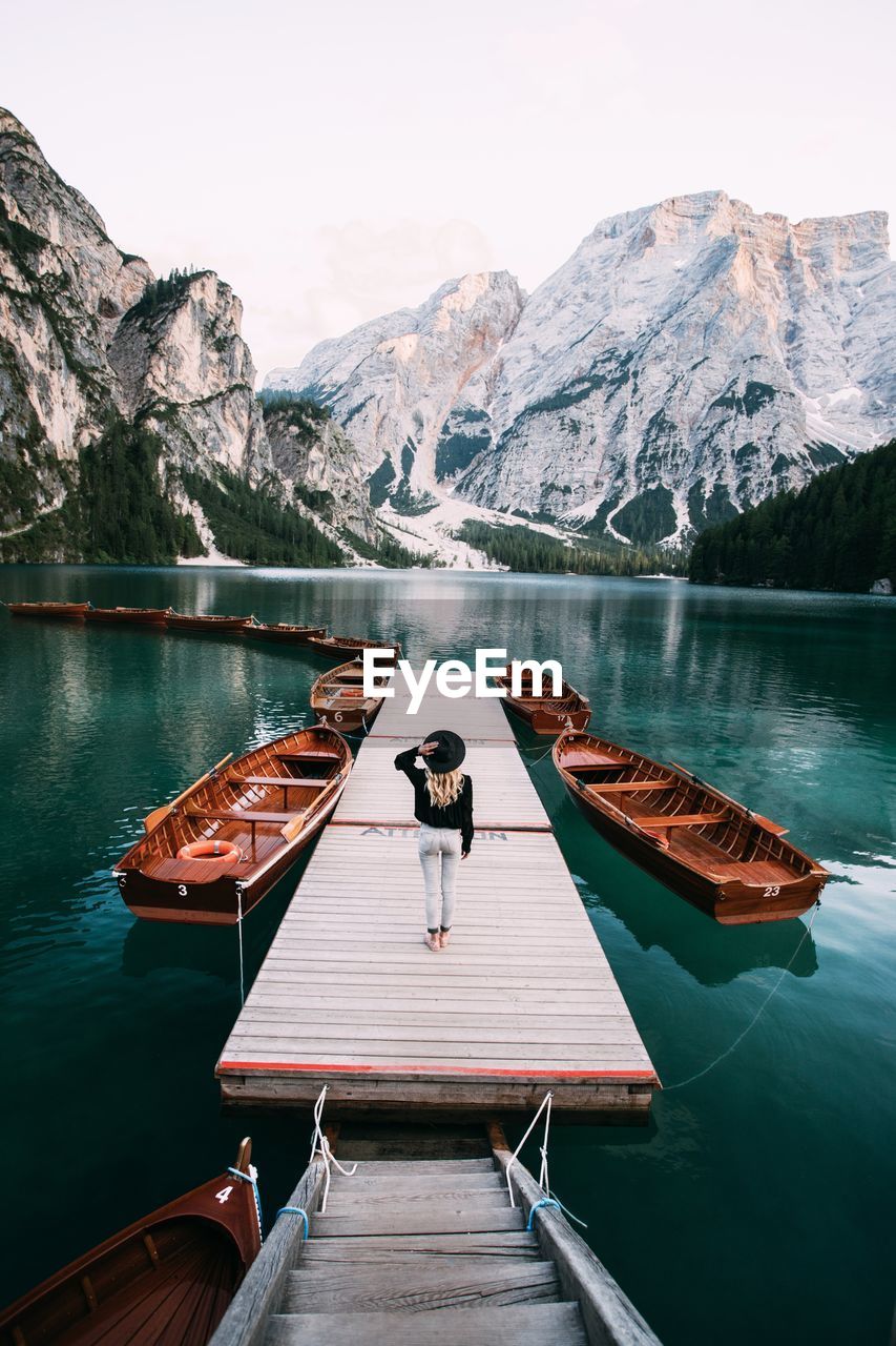 Rear view of woman walking on pier over lake against sky