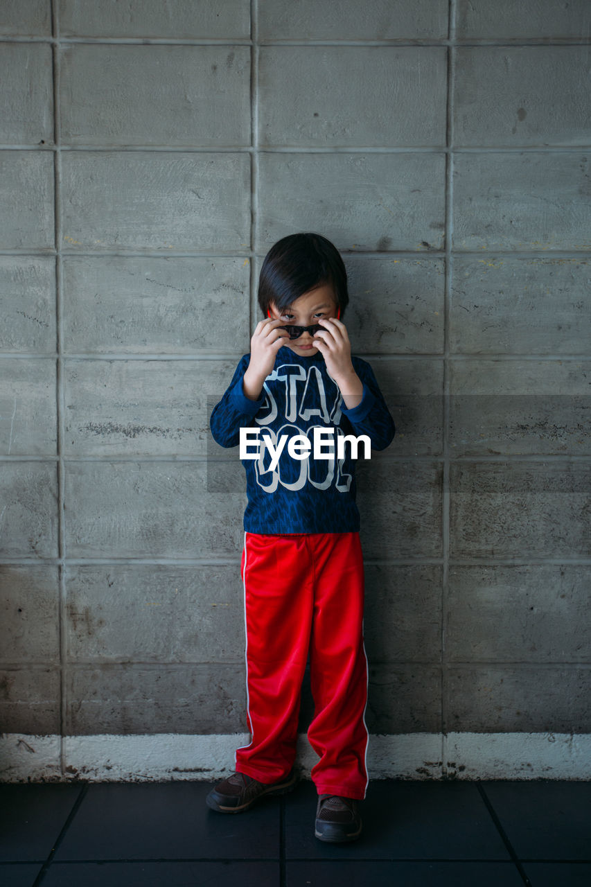 Full length portrait of boy in sunglass standing against wall