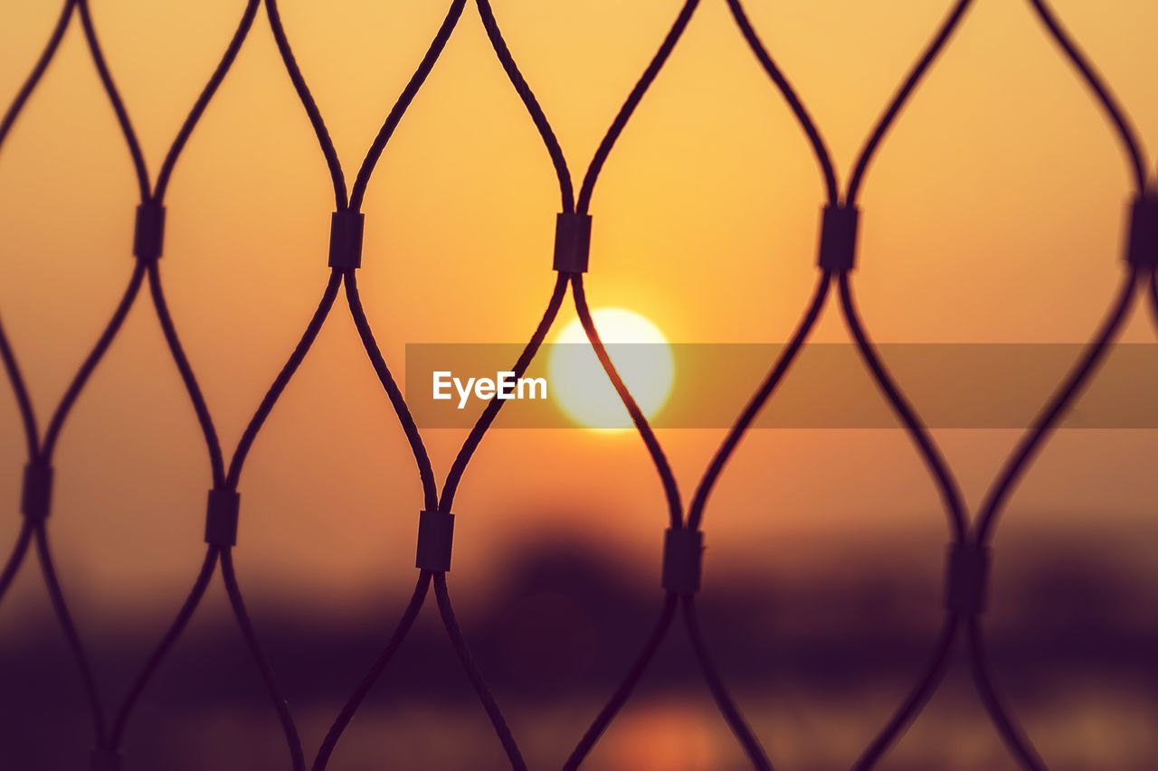 Silhouette chainlink fence against sky during sunset