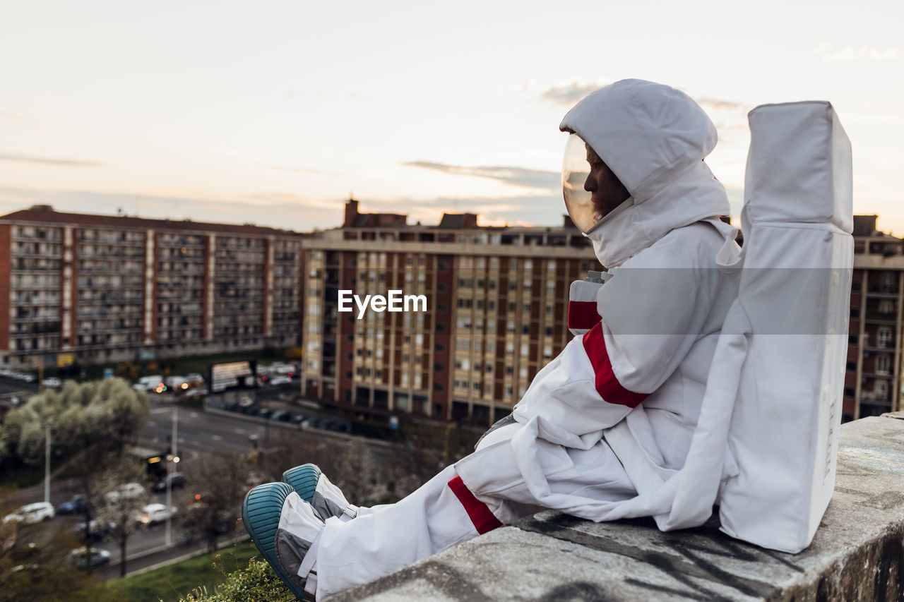 Young female astronaut sitting on retaining wall during sunset