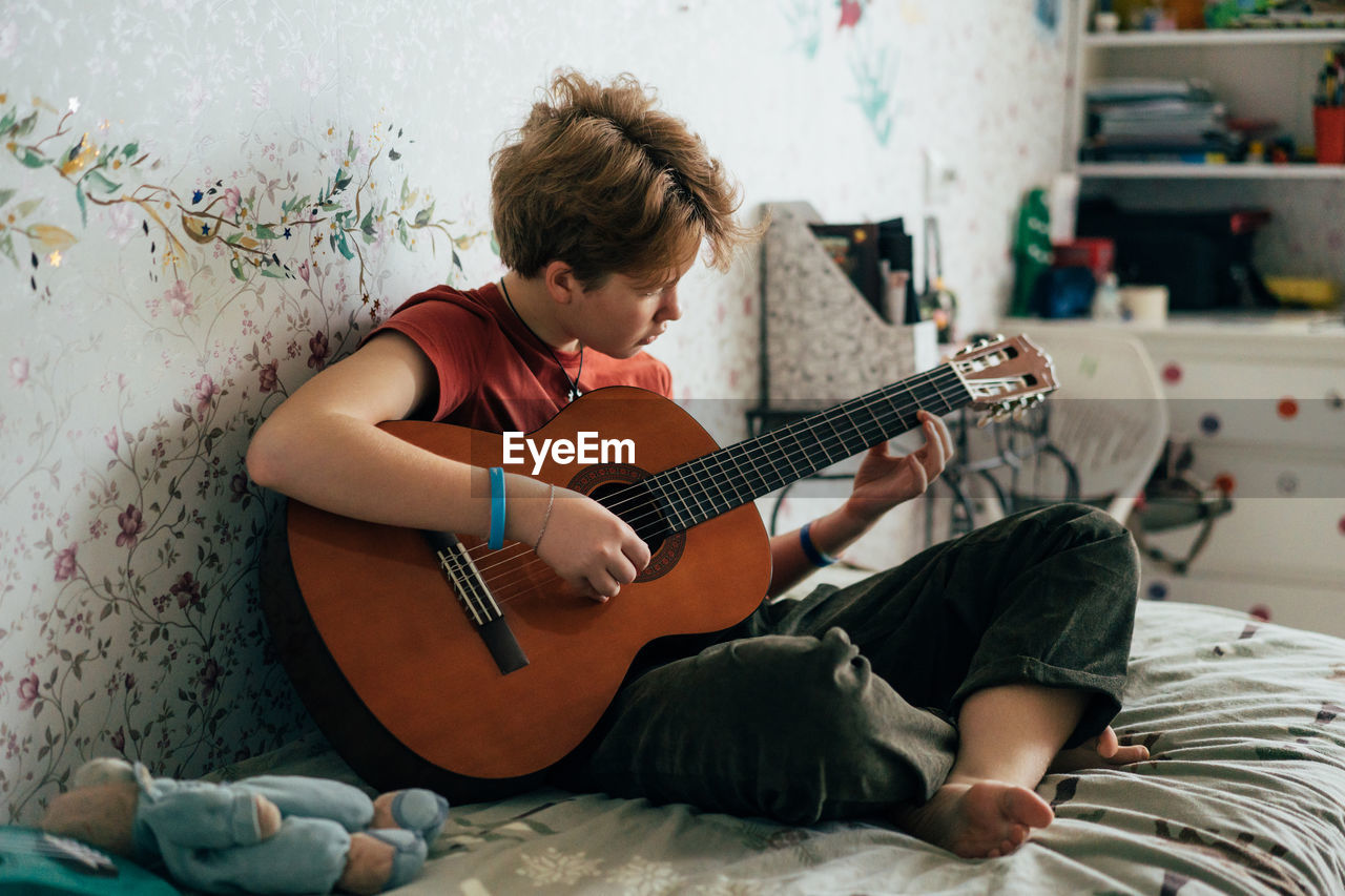 Romantic adolescent redhead girl learning to play the guitar while sitting in the room.