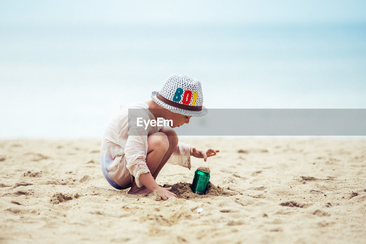 Rear view of boy sitting at beach against sky