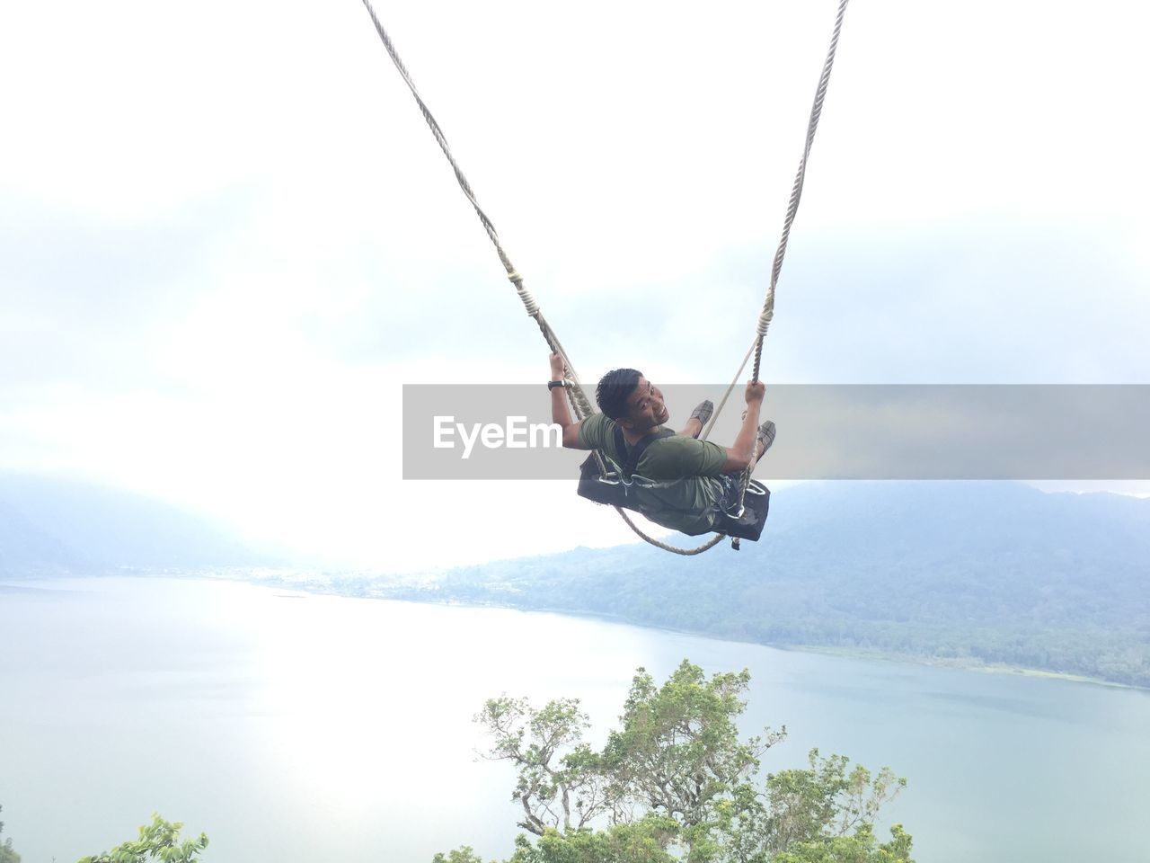 Man jumping on swing against sky