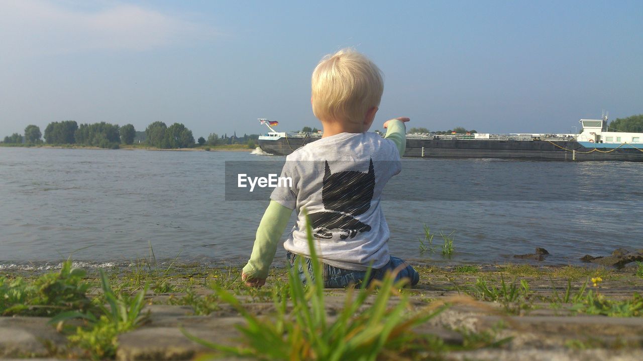 Rear view of boy pointing at lake against sky