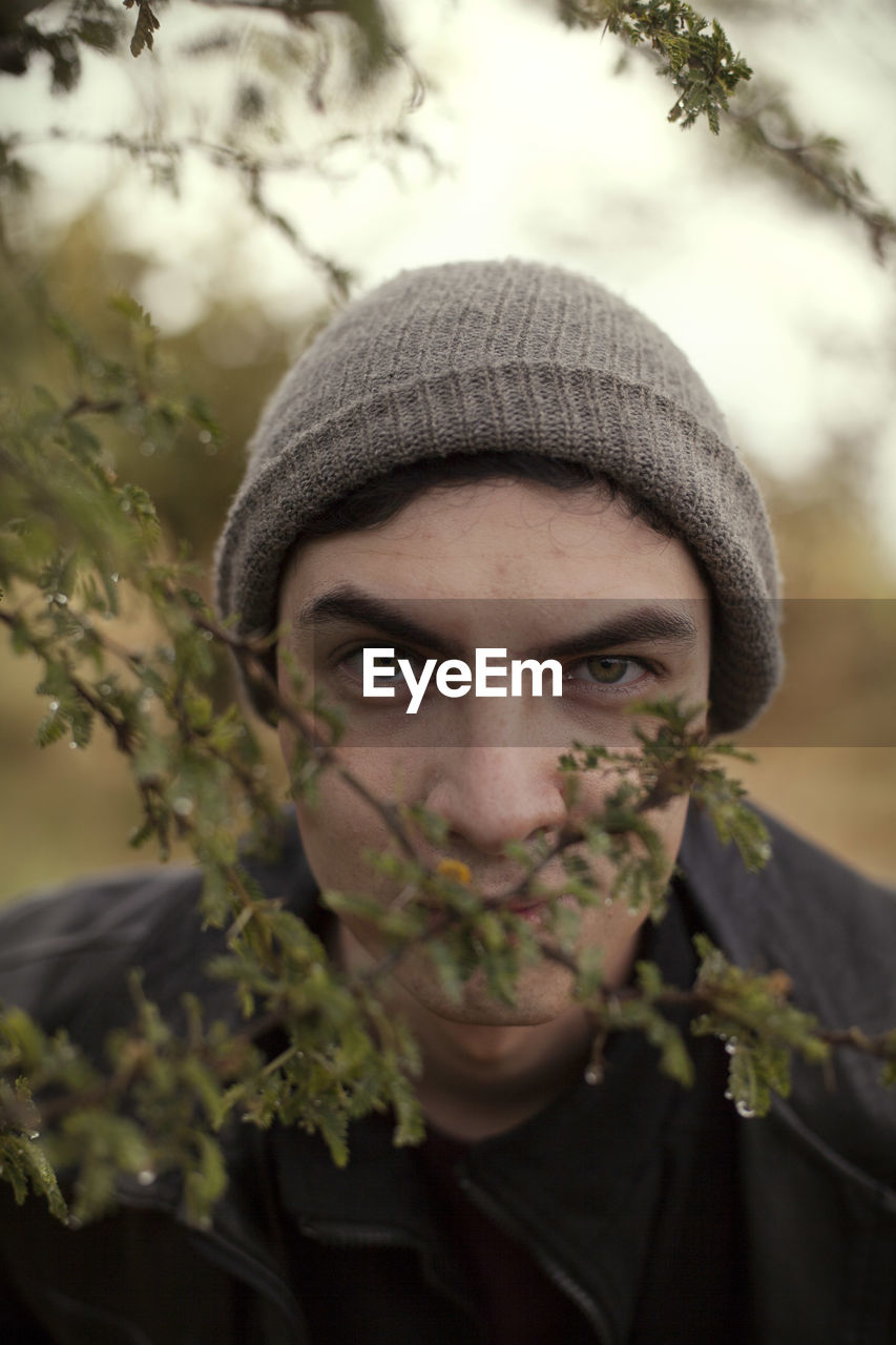 Close-up portrait of young man wearing hat by branch