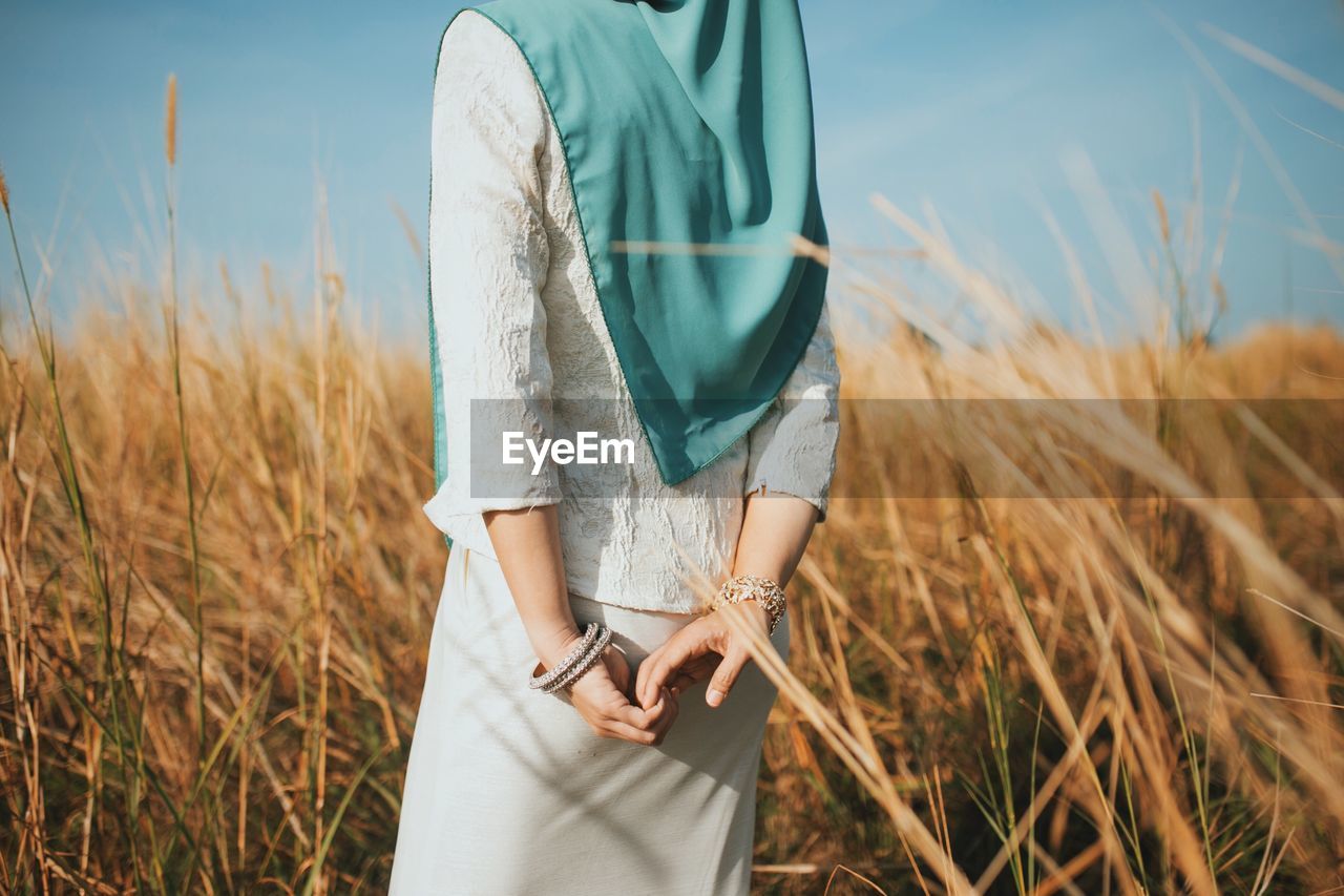 Midsection of woman standing on field against sky