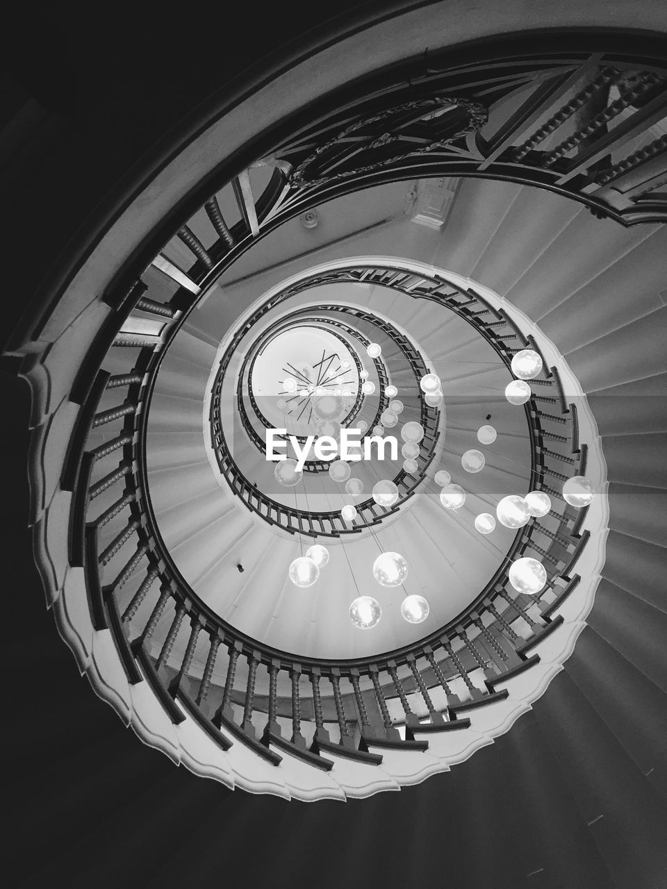 Low angle view of illuminated light bulbs hanging amidst spiral staircase