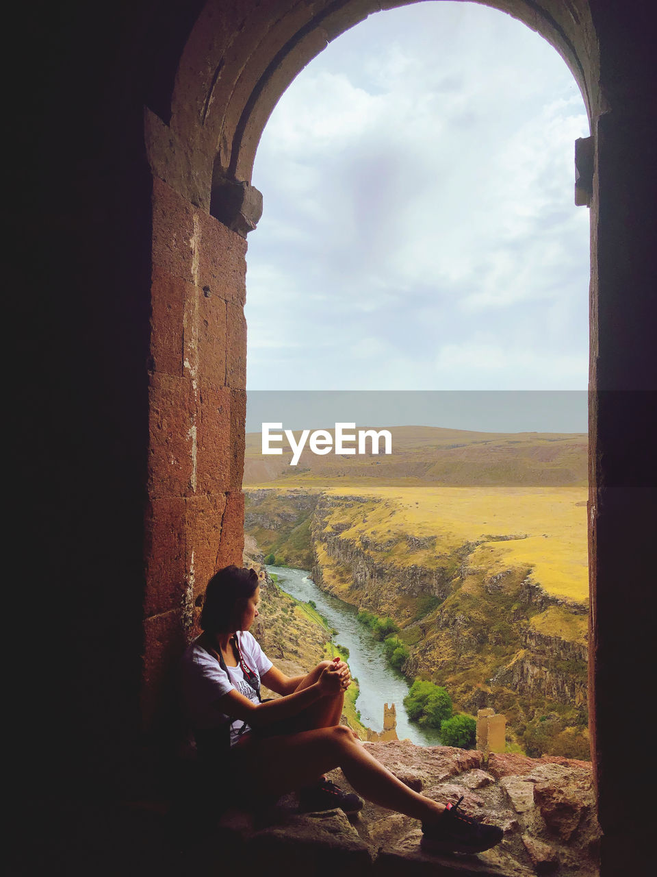 Woman sitting on arch window looking at mountains