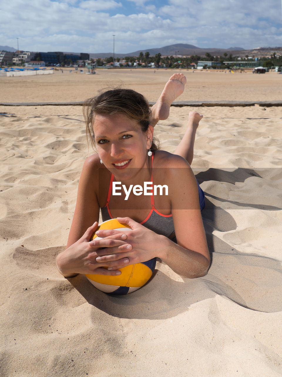 Portrait of woman lying with volleyball on sand at beach