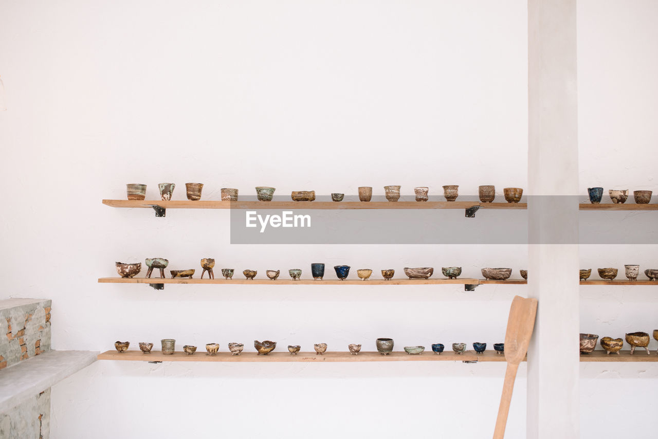 Cup and bowls on shelf against wall