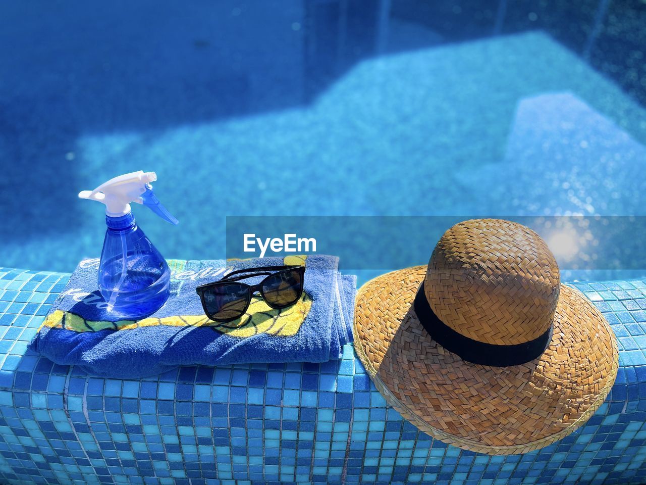 Straw hat, sunglasses, towel and bottle on the pool edge