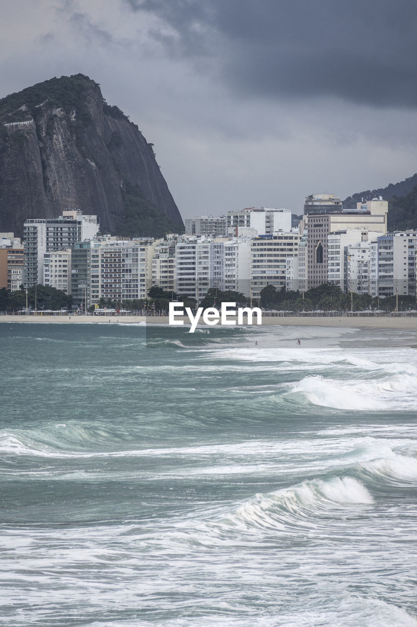 Beautiful view to waves crashing on the sand, buildings and mountains