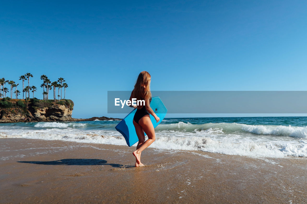 Young woman walking towards shore while carrying paddleboard