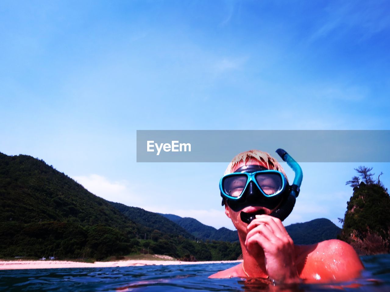 Close-up of young man snorkeling in sea against blue sky