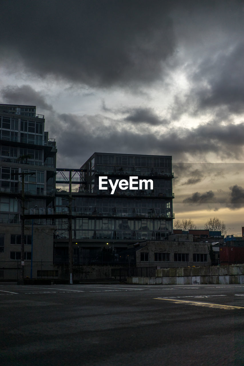 Low angle view of buildings in front of road against cloudy sky at dusk