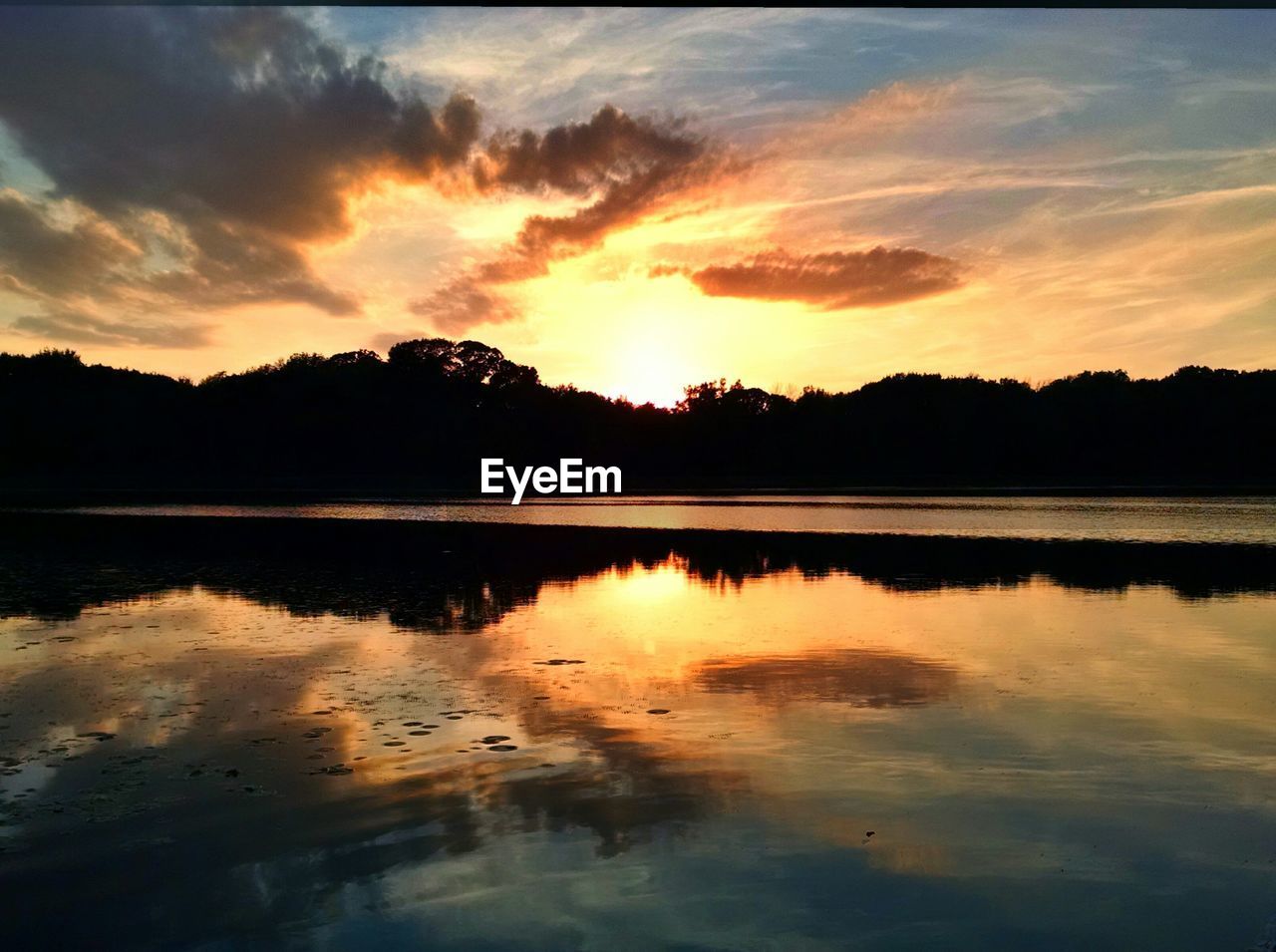 Scenic view of lake by silhouette trees against sky during sunset