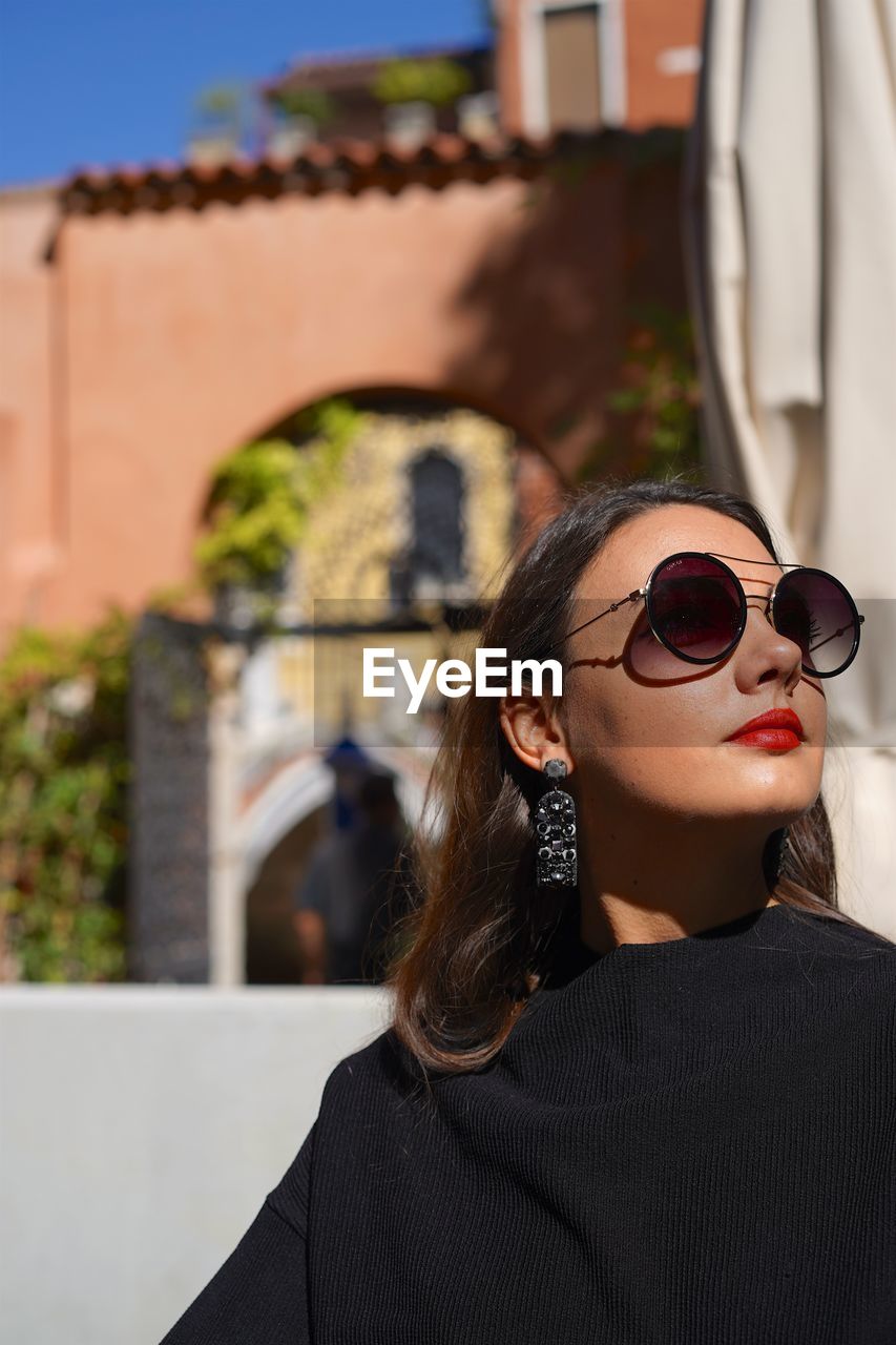 Young woman wearing sunglasses while standing against buildings