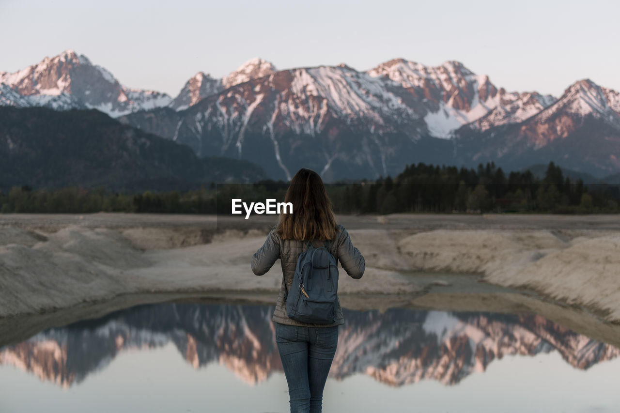 REAR VIEW OF WOMAN STANDING ON SNOWCAPPED MOUNTAIN