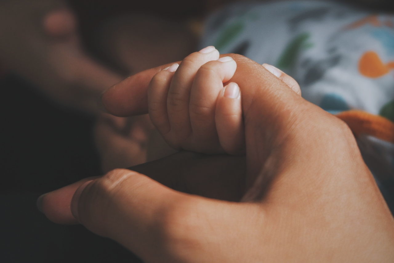 Cropped image of parent and baby holding hands on bed
