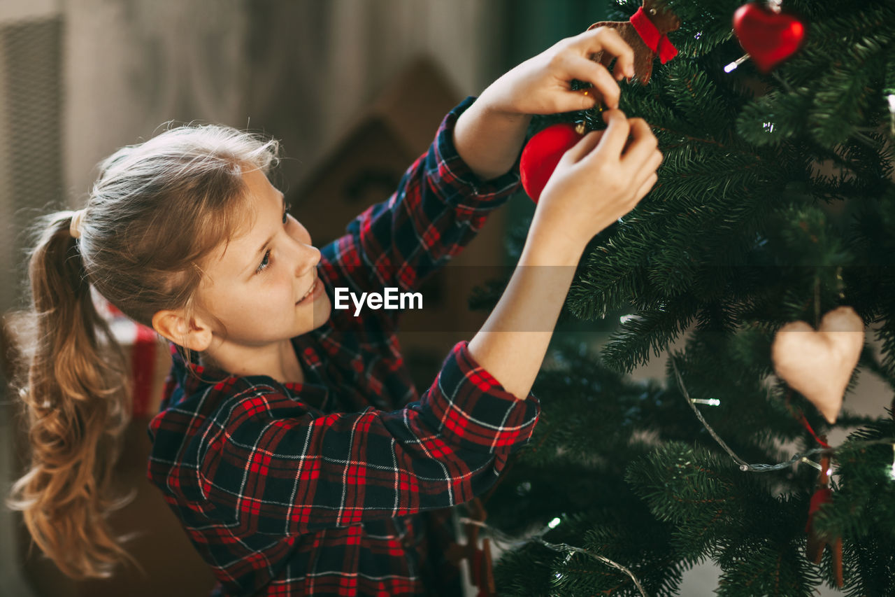 Happy little blonde in new year's home clothes, decorates the christmas tree and smiles. 