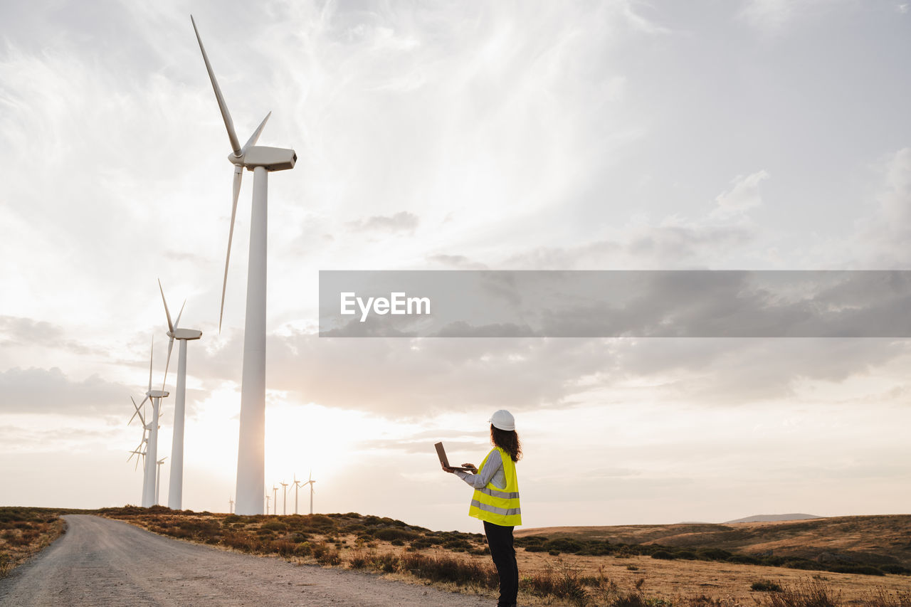 Engineer looking at wind turbines at wind farm on sunset