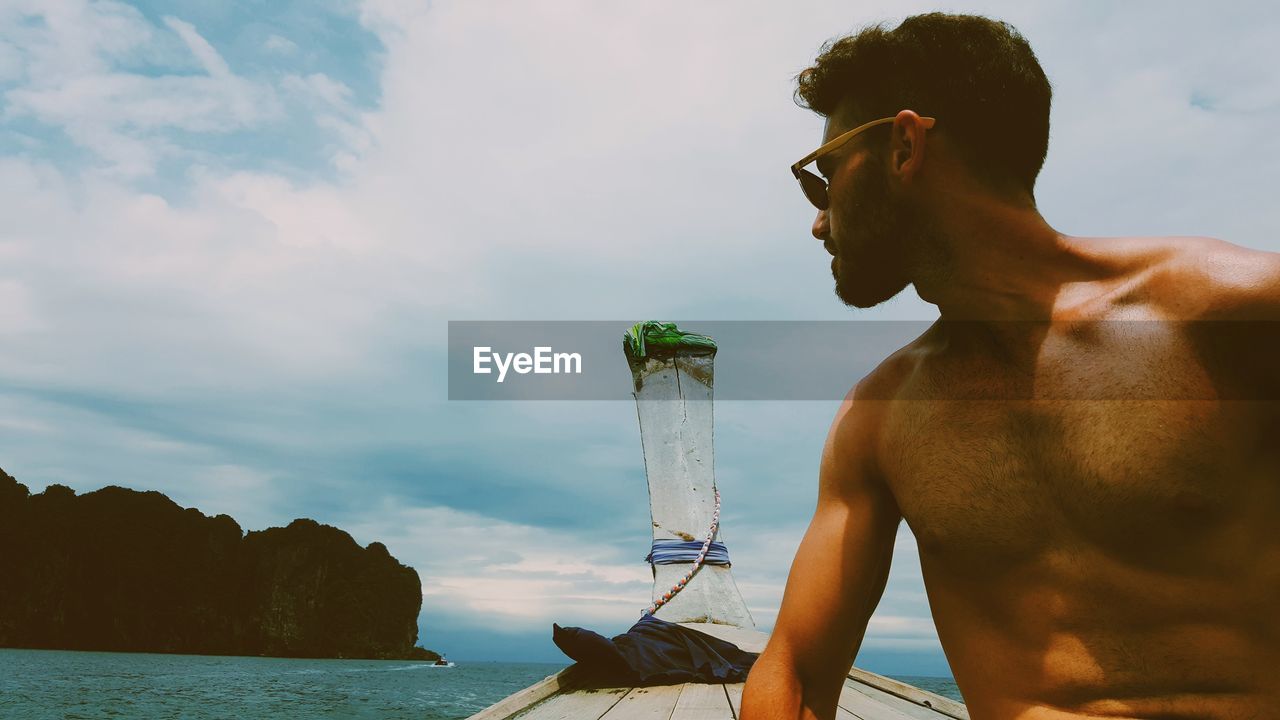 Shirtless man traveling in longtail boat on sea against sky