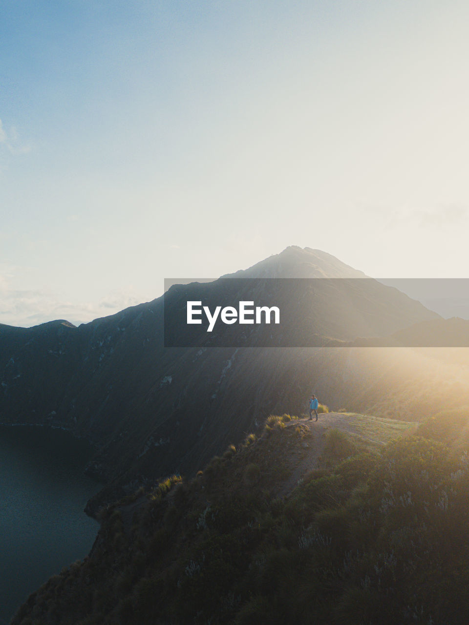 Man standing in the mountains with sunlight and lake