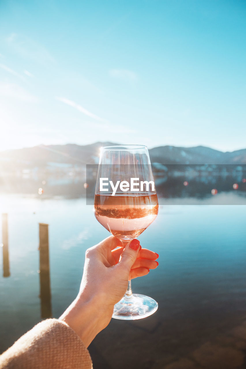 Female hand with glass of rose wine. cozy pier on the coast of lake tegernsee. mountains in bavaria