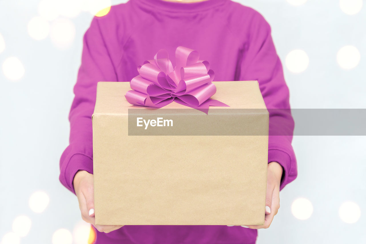 Gifts in woman's hands. a young woman in a violet sweatshirt holds a cardboard boxes with bow. 