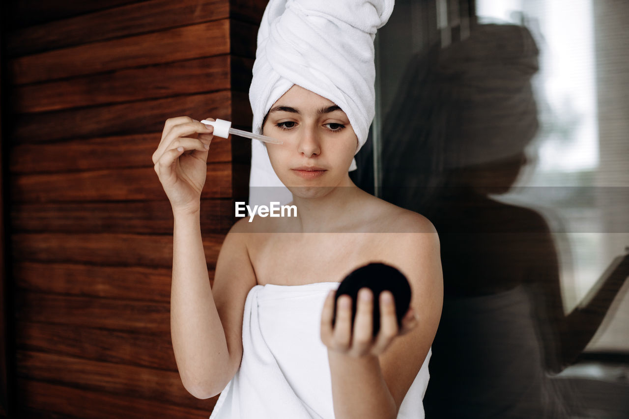 Young girl with towel on her head makes facial treatments. skin care, moisturizing with serum