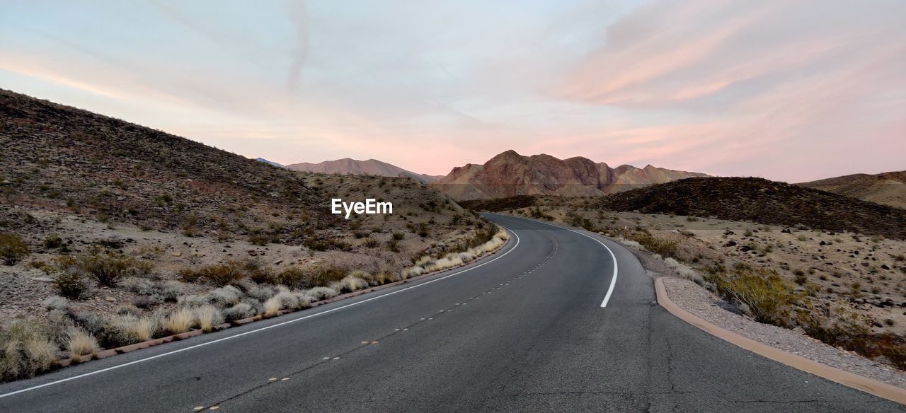 Empty road leading towards mountains against sky