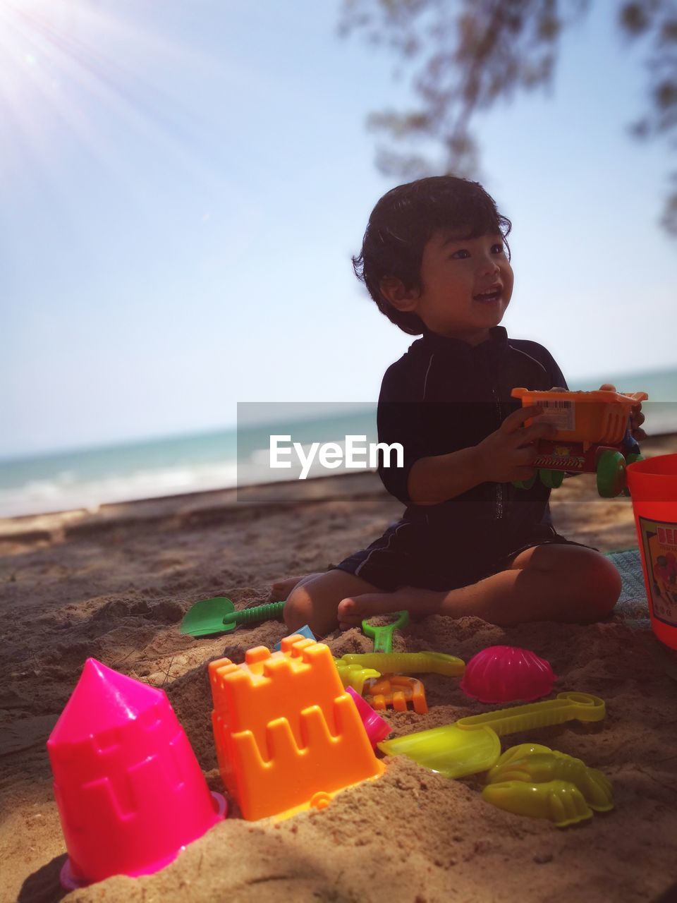 Boy playing with toys while sitting at beach against sky