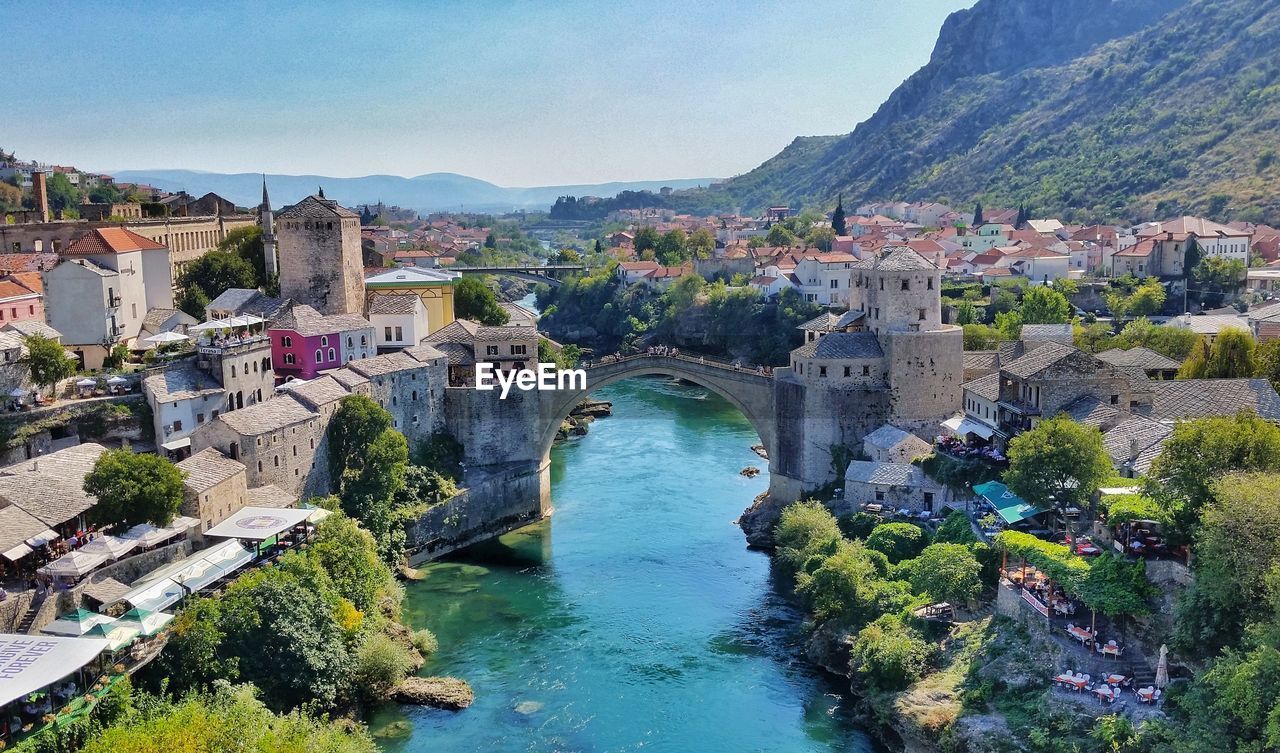 HIGH ANGLE VIEW OF BRIDGE OVER RIVER AMIDST BUILDINGS