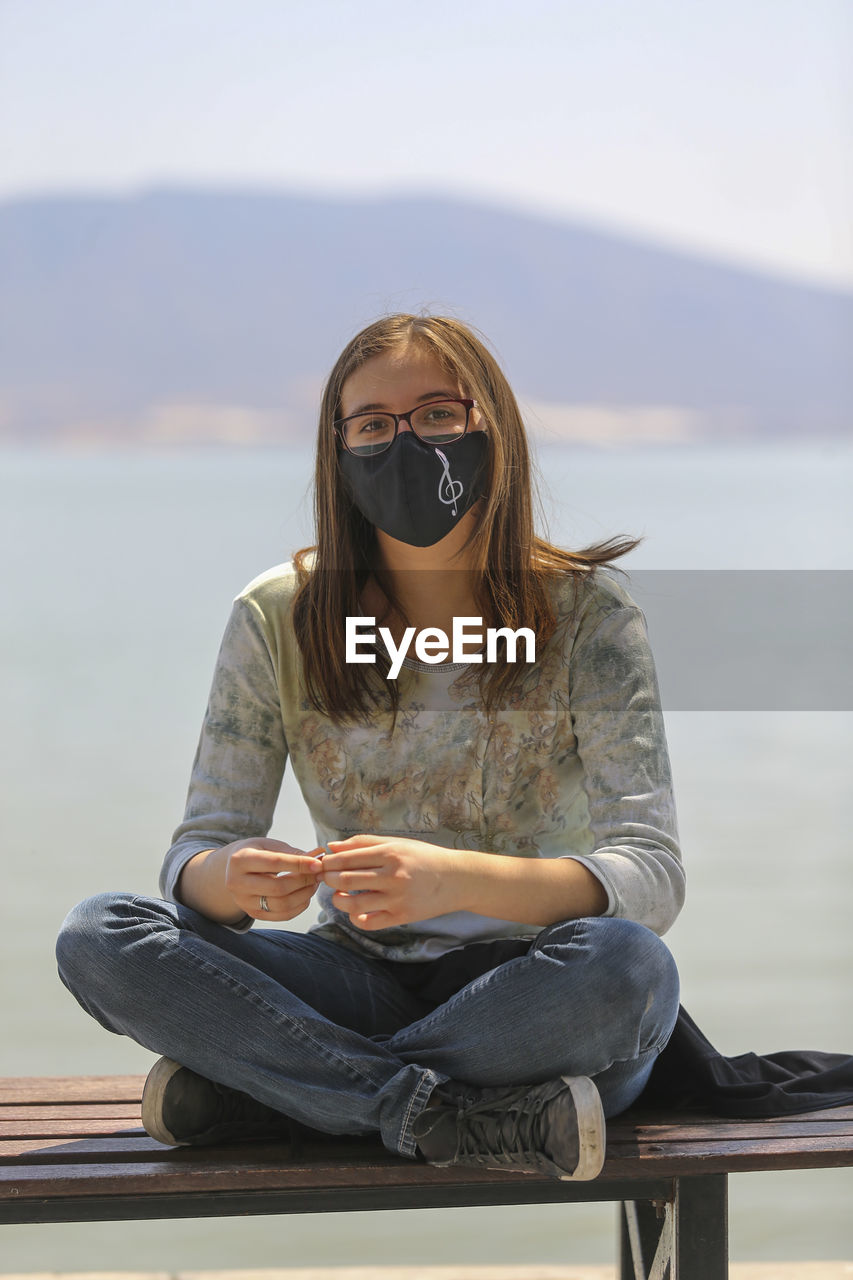 portrait of woman wearing sunglasses while sitting on bench