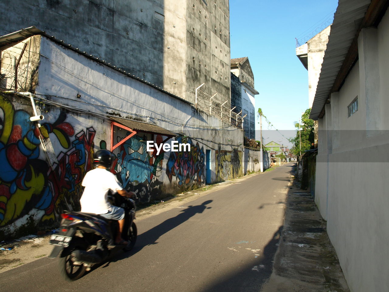 Rear view of man riding motorcycle on street by graffiti wall