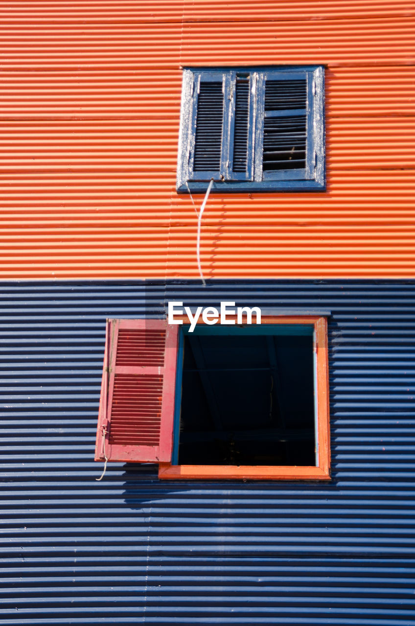 Low angle view of shuttered windows on two toned colourful corrugated iron building exterior. 