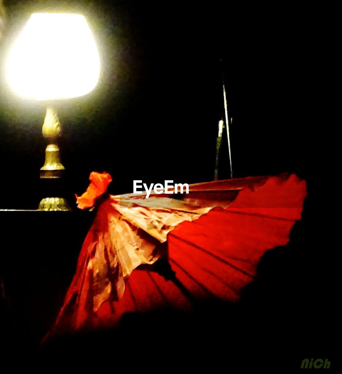 Close-up of drink umbrella by illuminated lamp shade in darkroom