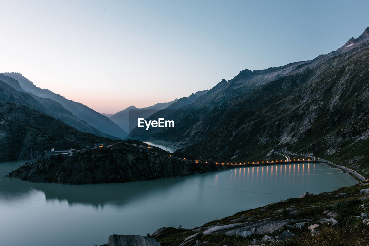 Scenic view of dam by mountains during sunset