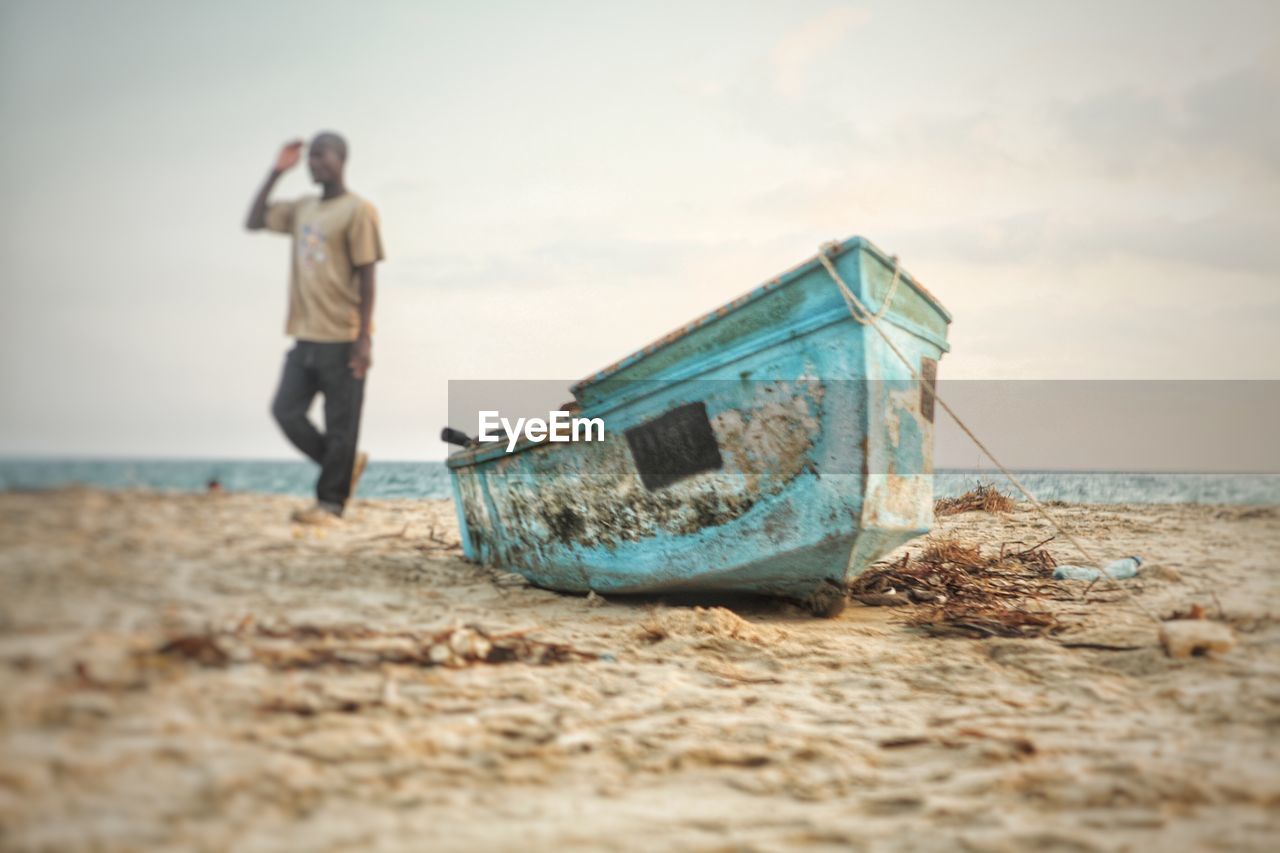 Man saluting while standing by boat at beach against sky