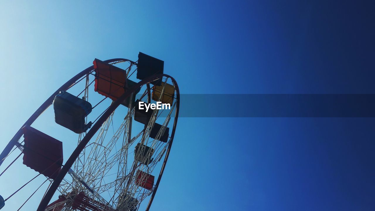 Low angle view of ferris wheel against clear blue sky