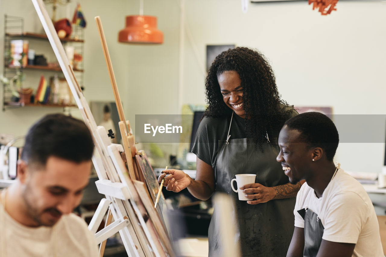 Cheerful female tutor with young student in front of painting in art class