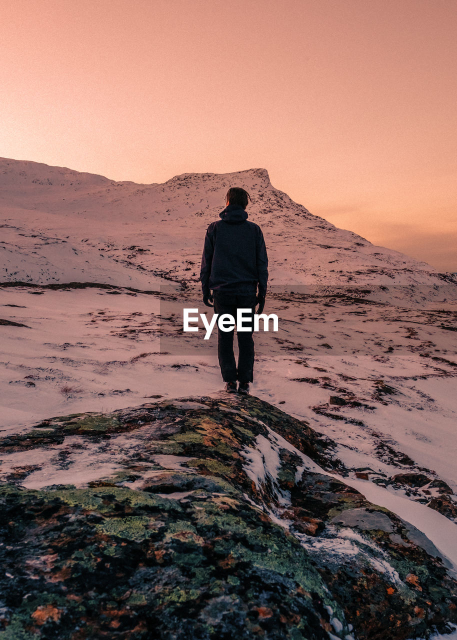 Rear view of man standing on snowcapped mountain against sky