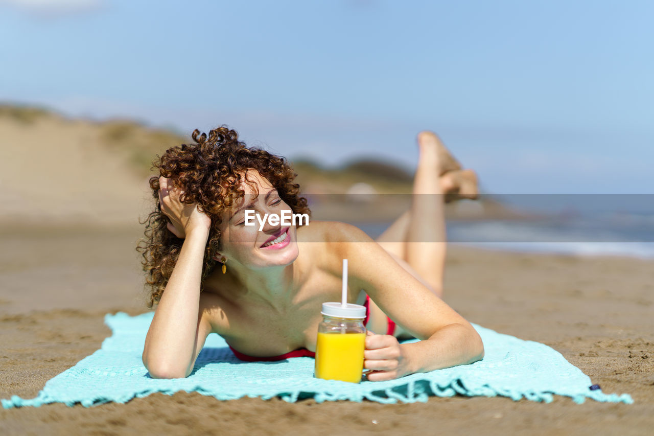 side view of woman drinking water at beach against sky